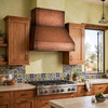 Modern hacienda kitchen with wide-chimney under-cabinet copper range hood between wood cabinets and Talavera tile