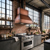 Industrial loft kitchen with wide-chimney under-cabinet copper range hood between reclaimed wood and brick wall