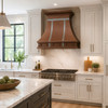 Hammered copper bell range hood with zinc straps in transitional kitchen with Shaker cabinets and marble