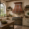 Hammered copper bell range hood with zinc straps in rustic European kitchen with plaster, timber and stone