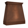 Angled front view of wall-mount hammered copper range hood with straight taper, brick apron, and crown