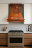 Country kitchen copper exhaust hood in modern kitchen, curved copper canopy with warm rustic patina above clean cabinetry and stone surfaces
