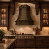 Faceted copper island range hood with riveted straps in a transitional kitchen with simple cabinetry and stone