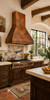 Custom tapered copper range hood in a Spanish Colonial kitchen with plaster, carved wood, beams, and tile