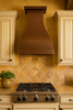 Large custom hammered copper kitchen range hood in Tuscan Italian kitchen, artisan copper canopy above stone backsplash and warm rustic cabinetry