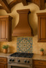 Large custom hammered copper kitchen range hood in Spanish style kitchen, artisan metal canopy above carved cabinetry and rustic beam ceiling