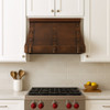Hammered copper range hood in transitional kitchen above range, warm patina finish with clean cabinetry and stone backsplash