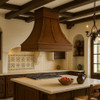 Central island copper range hood in Spanish Colonial style kitchen, hammered canopy above island with wood beams and stone backsplash