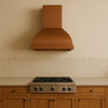 42-inch hand-hammered barrel copper hood above stove in a farmhouse kitchen with Shaker cabinetry and honey patina