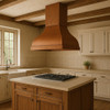 Wall-mount barrel shape copper range hood in a farmhouse kitchen with Shaker cabinetry, wood ceiling beams and rich copper tones