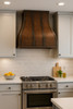 Spanish Colonial hammered copper range hood in contemporary kitchen, warm patina canopy above clean cabinetry and modern stone surfaces
