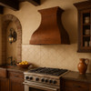 Handcrafted copper range hood with flared bell silhouette in Spanish colonial kitchen setting