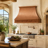 Hammered copper exhaust hood in a Tuscan kitchen with stone backsplash, dark wood cabinetry, and grapevine apron