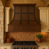 Rustic copper range hood with grapevine apron and straps in Tuscan style kitchen, hammered copper canopy above stone walls, rustic cabinetry and warm Mediterranean accents