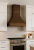 Luxury copper range hood with wide apron and small crown molding in traditional kitchen, hammered copper canopy above classic cabinetry and stone backsplash