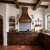 Hammered bell copper range hood with broad apron in Spanish Colonial Revival kitchen with Saltillo tile and plaster walls