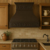 Farmhouse copper range hood with decorative scroll apron in country style kitchen, hammered bell canopy with warm antique patina above rustic cabinetry