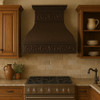 Farmhouse copper range hood with decorative scroll apron in southeastern style kitchen, hammered bell canopy with warm antique patina above spacious cabinetry