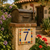 Talavera tile plaque number seven with Mexican floral border attached to a rustic mailbox in a landscaped outdoor setting