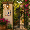 Talavera tile plaque number five with Mexican floral border installed near a decorative garden gate with flowering greenery