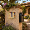Talavera tile plaque number one with Mexican floral border mounted on a rustic mailbox pillar at a countryside residence entrance