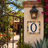 Talavera tile plaque number zero with Mexican floral border installed near a garden gate with stucco walls and flowering plants