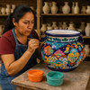 Talavera flower planter with colorful hand-painted design being painted by a Mexican artisan in her studio