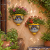 Yellow and cobalt wall sconces with flowering plants displayed on a sunny garden wall