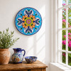 Colorful floral decorative talavera plate with blue scrollwork design displayed on a white wall beside a sunlit window