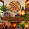 Yellow floral decorative talavera plate with blue lattice design mounted above a rustic fireplace in a cozy interior