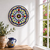 Traditional geometric decorative talavera plate with floral Mexican motifs displayed on white walls beside a sunlit window in a bright Spanish-inspired interior.