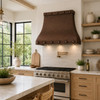 Hammered curved apron copper range hood in a bright California transitional kitchen with white oak cabinetry and large windows