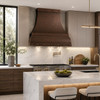Hammered curved apron copper range hood in a luxury contemporary kitchen with minimalist cabinetry, marble, and warm wood accents
