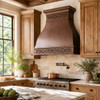 Rustic kitchen with hammered copper range hood, scroll bands, wood cabinetry, stone counters, and warm aged finish