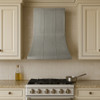 Smooth zinc range hood with refined bell silhouette in a Mediterranean kitchen with cream cabinets