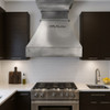 Zinc range hood with stepped crown molding in a European modern farmhouse kitchen with plaster walls, natural stone backsplash, and aged hardware