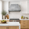 Angled view of a minimalist smooth zinc range hood with tapered silhouette in a transitional style kitchen