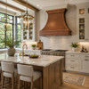 Wall-mount hammered copper bell range hood in a transitional kitchen with Shaker cabinetry and quartzite