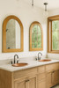 Two arched hand-hammered copper mirrors obove two drop-in copper sinks in a modern rustic bathroom