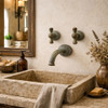 Rustic oxidized brass wall faucet with dual paddle handles in a rustic bathroom