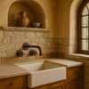Brass cross handle wall faucet in Tuscan kitchen with plaster walls and arched niche backdrop.