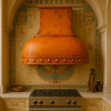 Dome shape copper range hood in Egyptian style kitchen, rounded hammered canopy with warm patina above range and arched details