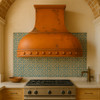 Dome shape copper range hood in Moorish style kitchen, rounded hammered canopy with warm patina above range and arched tile details