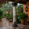 Weathered stone column with ornate swirl capital in a hacienda garden with clay pots and flowers
