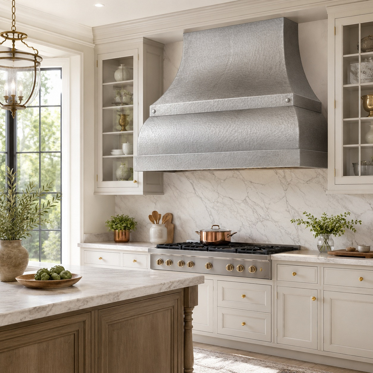 Hammered zinc bell range hood with band and boxed apron in European kitchen with painted cabinets, stone, timber, and plaster