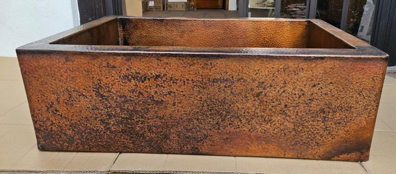Front view of rustic hammered copper apron-front single-bowl sink with patina