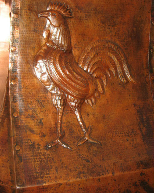 Close up view of rooster motif on copper vent hood apron, raised decorative detail with hammered copper texture 