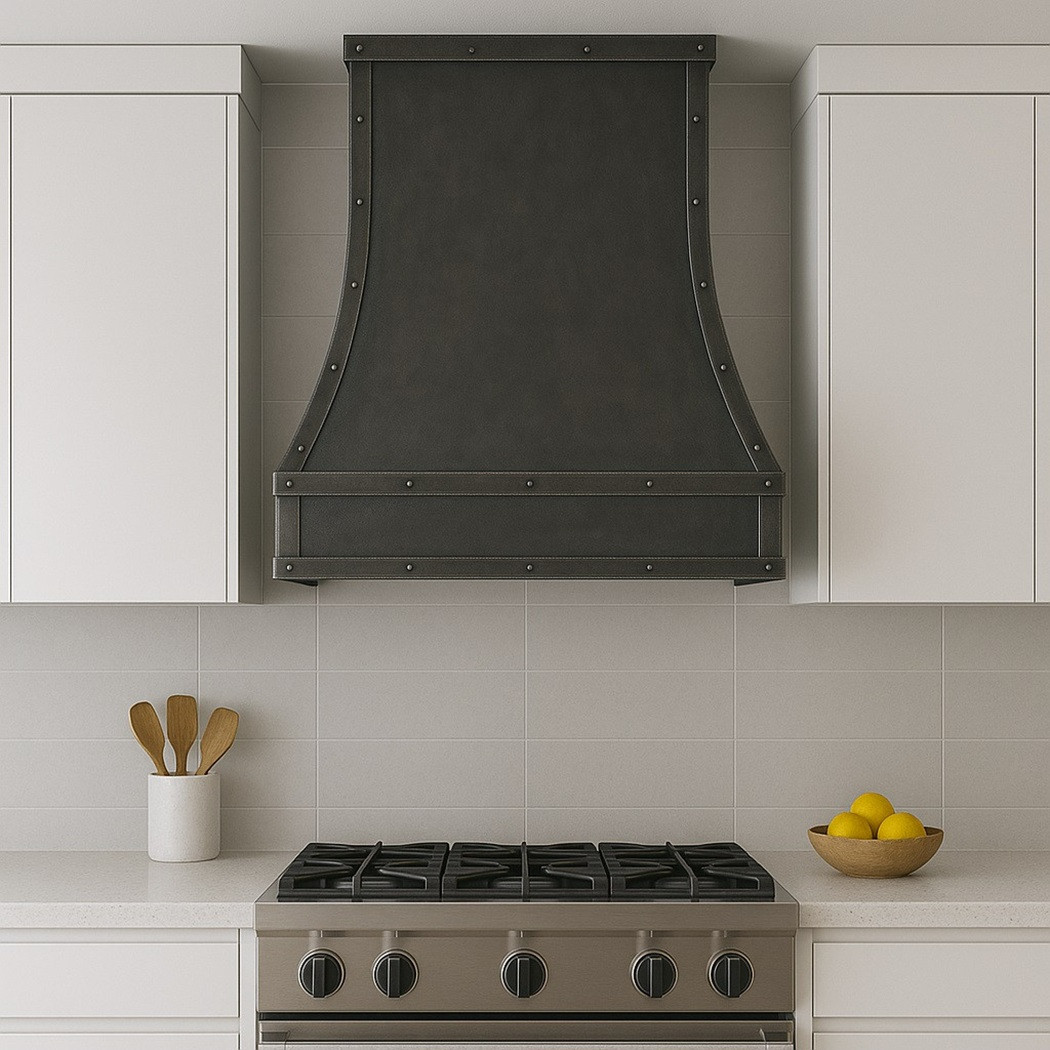 Dark zinc range hood with riveted vertical strap seams in an urban modern kitchen with white subway ceramic tiles and matte cabinetry