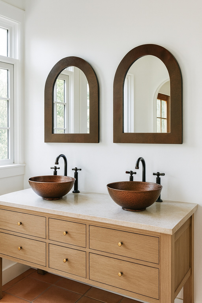 Arched hand-hammered copper mirror in a Southeastern style bathroom with two vessel sinks and terra cotta floor