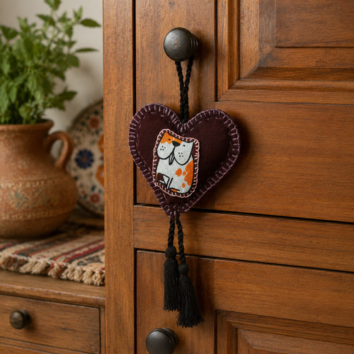 Handmade Mexican heart ornament with cat motif hanging from a rustic wooden cabinet pull